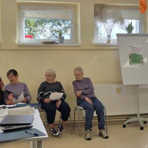 Uczestniczki rozmawiają przy flipcharcie z plakatem „uMOCnieni w kryzysie”; w tle okna i dekoracje.