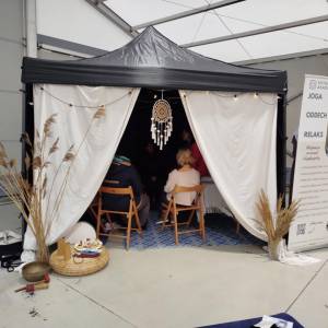 Namiot warsztatowy „Avitale Akademia Oddechu”. Uczestnicy siedzą w środku; na roll-upie hasła: joga, oddech, relaks.