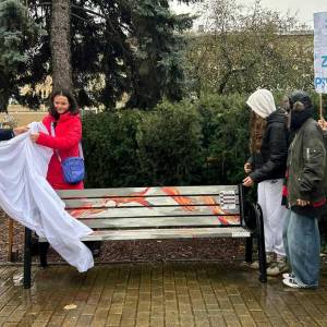 Grupa osób odsłania kolorową „Ławkę Dobrych Słów” w parku podczas Światowego Dnia Zdrowia Psychicznego; na mokrym chodniku widać ławkę z ilustracją i tabliczką informacyjną.