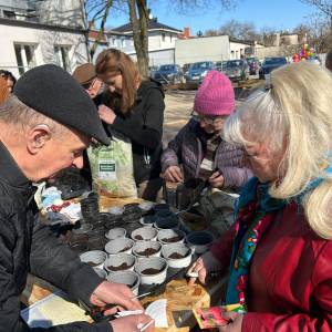 Uczestnicy przygotowują doniczki i nasiona przy stole podczas wiosennych zajęć ogrodniczych.