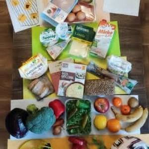 Produkty spożywcze, owoce, warzywa i artykuły pełnoziarniste ułożone na stole podczas warsztatów o piramidzie żywieniowej dla seniorów.