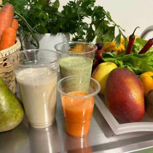 Świeże owoce i warzywa oraz przygotowane soki w plastikowych kubkach na stole podczas warsztatów dietetycznych dla seniorów