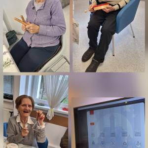 Seniorzy siedzą w sali i grają na prostych instrumentach perkusyjnych, korzystając z multimedialnych narzędzi podczas zajęć muzycznych.