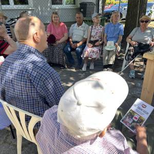Grupa osób słucha wykładowcy w ogrodzie społecznym Centrum Usług Społecznych w Swarzędzu.
