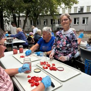Seniorki kroją pomidory i przekładają je do słoików podczas warsztatów przetwórczych.